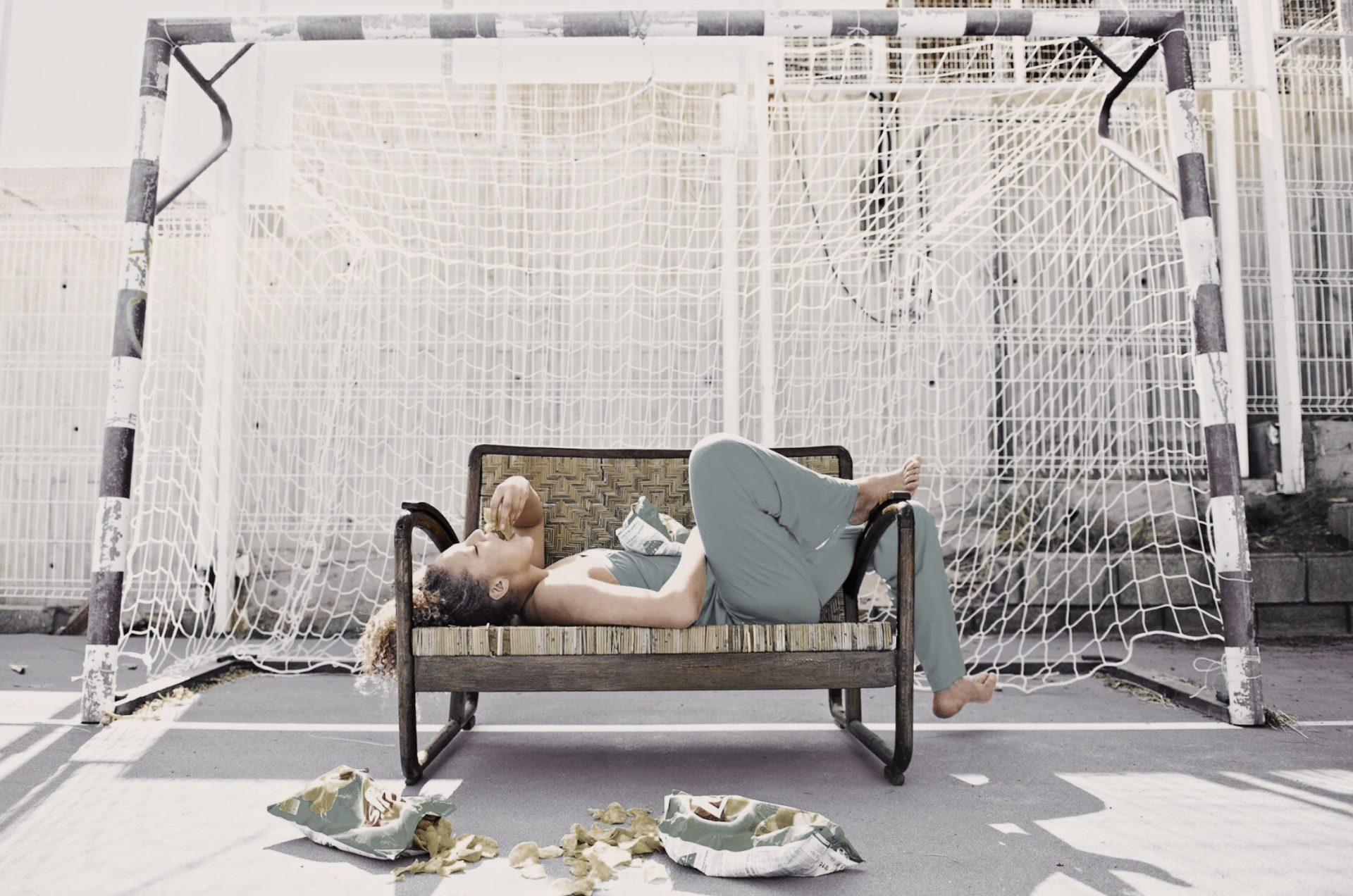 Processed with VSCO with dog1 preset Frau liegt auf einer sonnigen Bank und isst Chips im Hintergrund ein Fußballtor